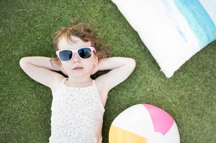 Little girl laying in sun on grass with toys.